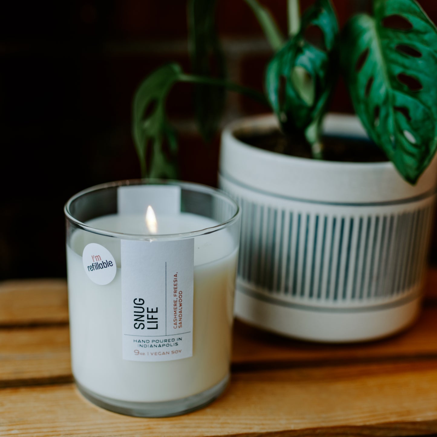 Refillable lit candle sitting next to a plant on a table. 