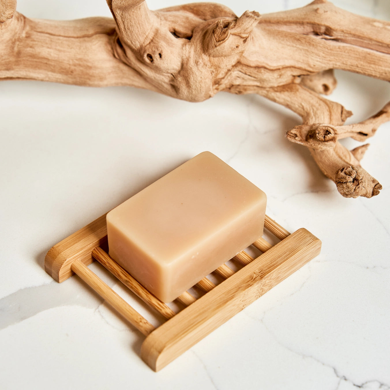 Bar of soap on a wooden soap dish with driftwood on a light background