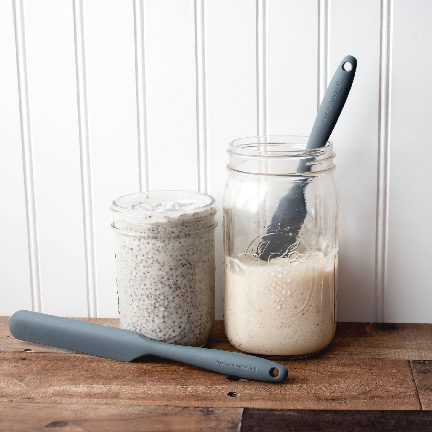 Two jars with food and a silicone spatula on a counter.