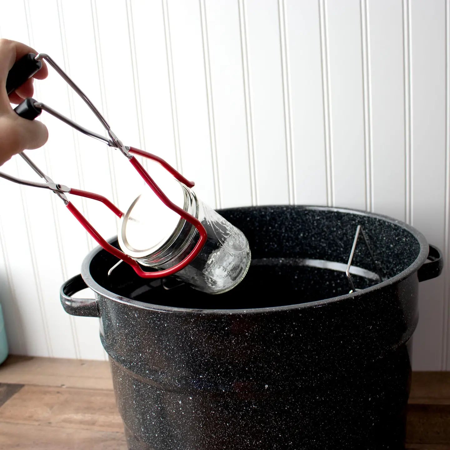 Person using canning jar tongs to pull jar from pot. 