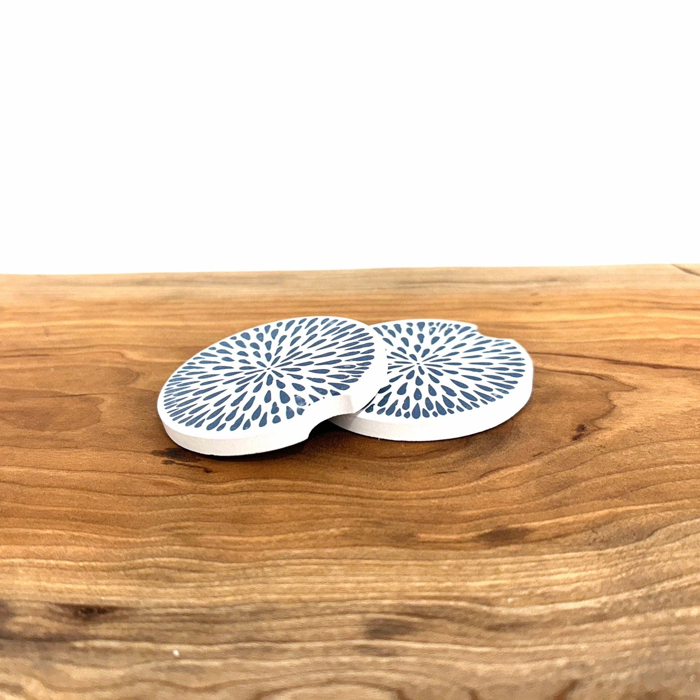 Two white car coasters with blue patterns on a wooden surface