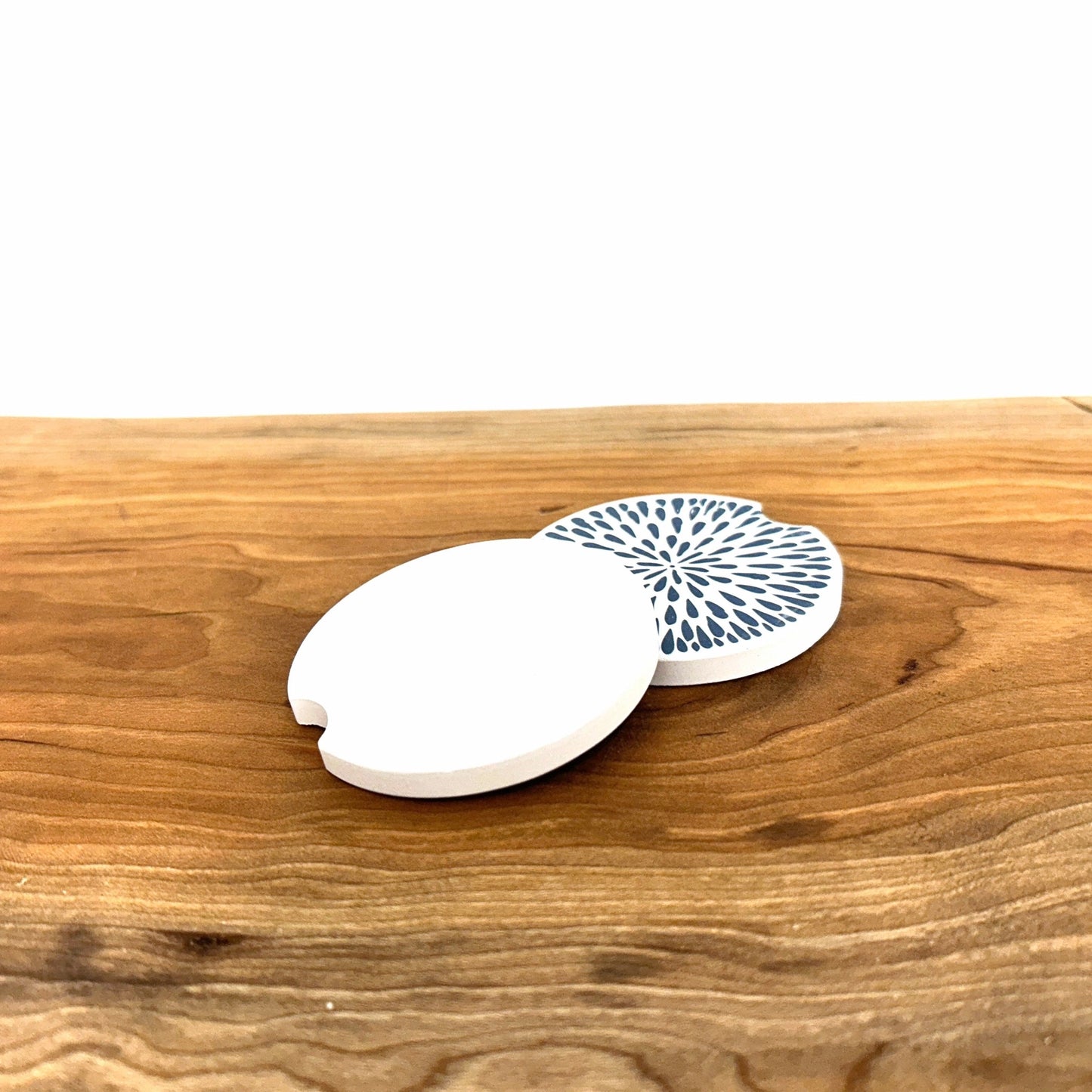 Two white coasters with blue patterns on a wooden surface