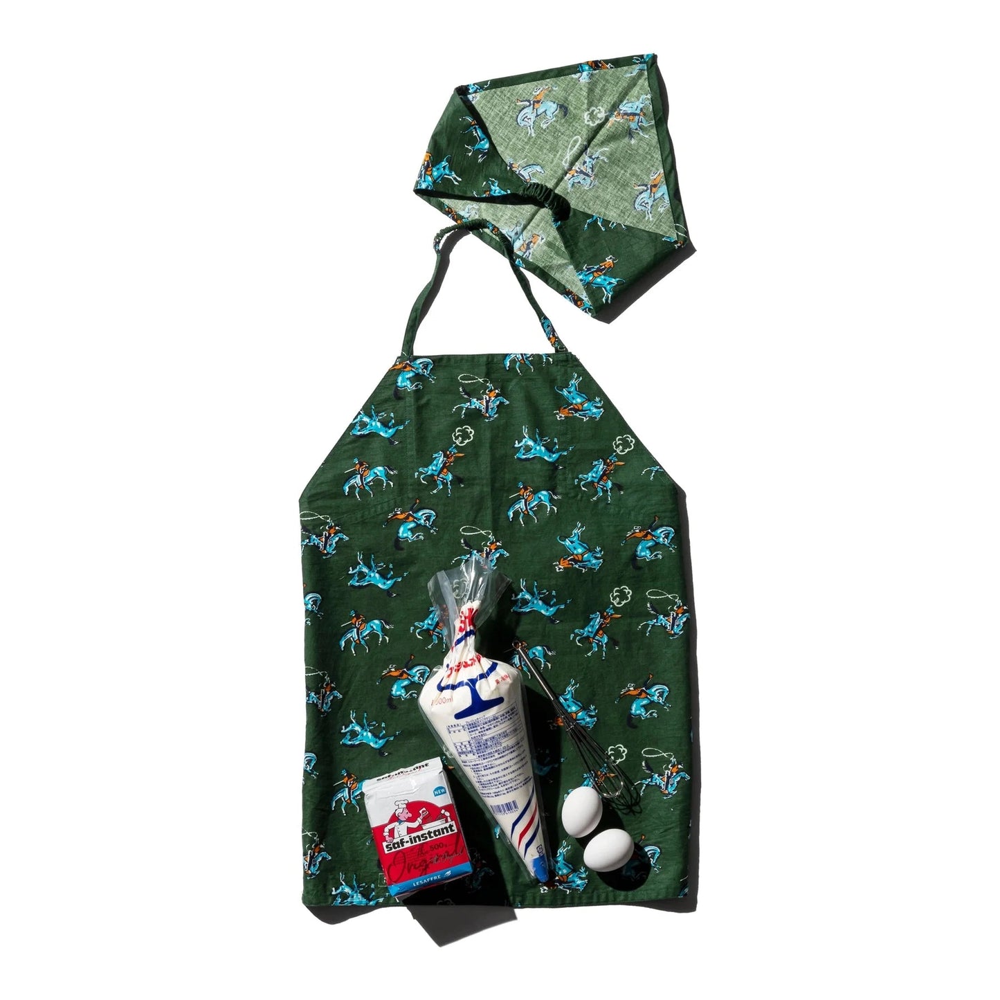 Green apron with cowboy pattern, hat, and baking supplies on a white background