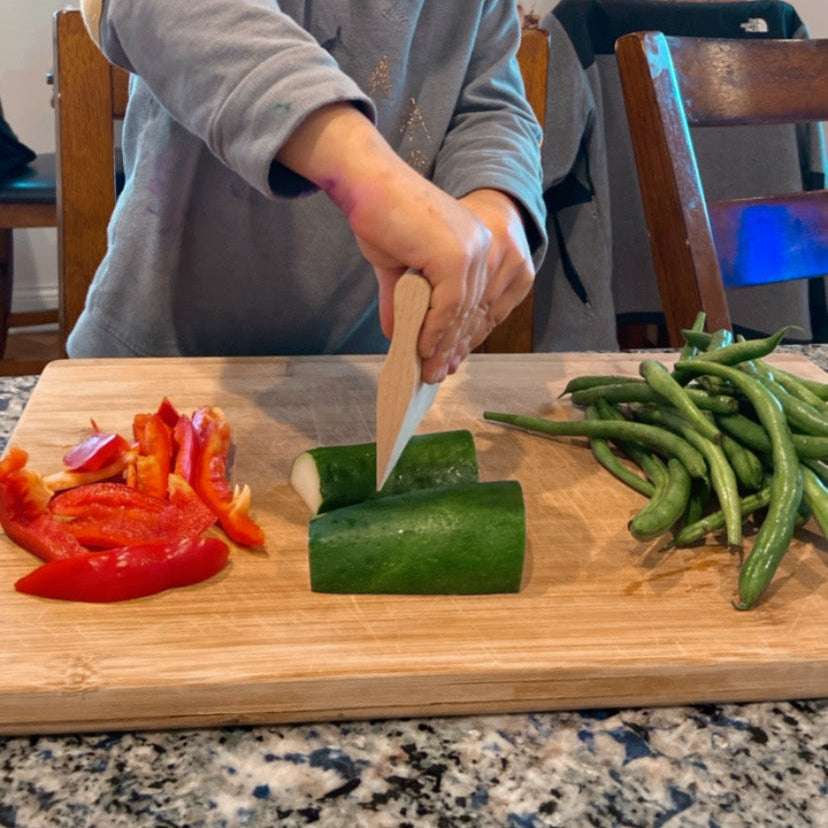 Kid cutting vegetables with wooden kitchen tool. 