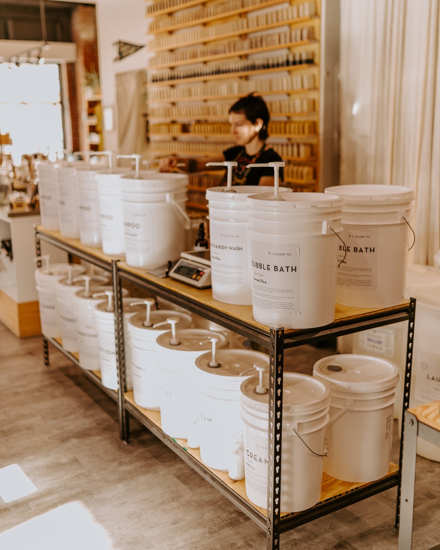 White buckets labeled 'Bath' on a metal shelf in a store setting.