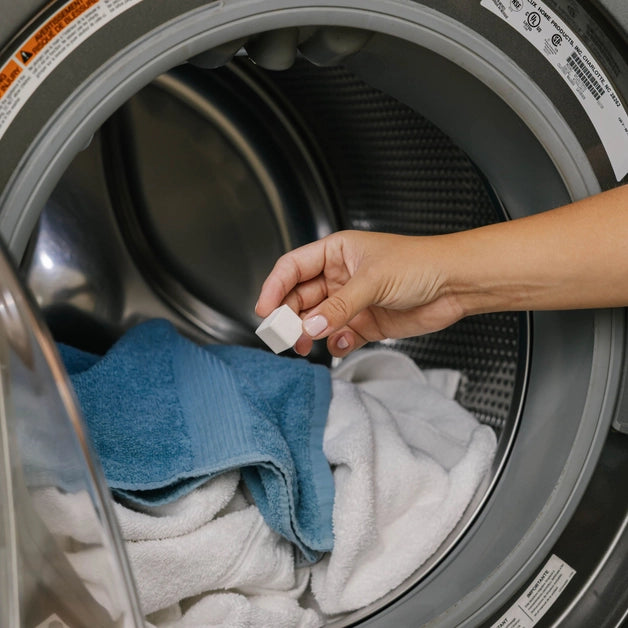 Hand adding detergent cube to a washing machine with clothes inside